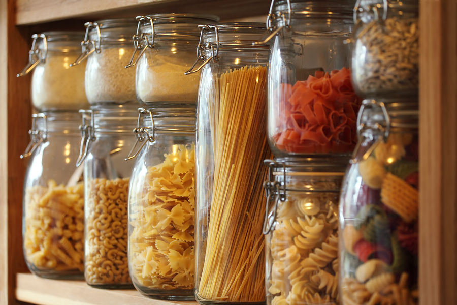 Photo of dried pasta in jars on a shelf in a domestic kitchen. Very shallow depth of field focusing on the middle jar.